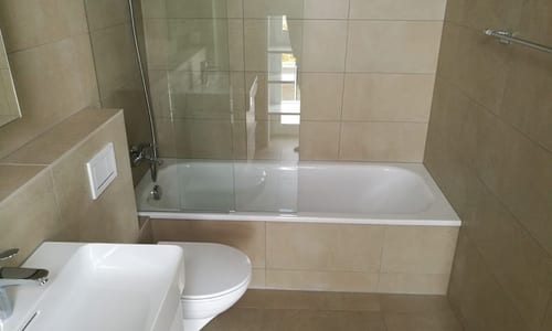 Kleines Badezimmer mit beigen Platten und weisser Badewanne